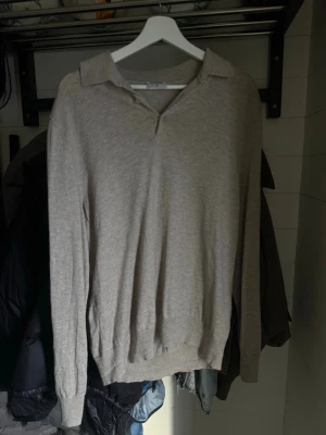 Beige tröja med krage från Filippa K - Stilren beige långärmad tröja från Filippa K med klassisk krage och v-ringning. Tröjan är i mjukt material och har ribbade muddar vid ärmslut och nederkant. Perfekt för en clean och avslappnad look.