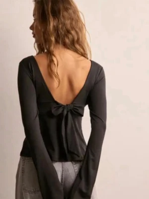 Svart långärmad topp med rosett bak - Säljer en svart långärmad topp med djup v-ringad rygg och en snygg rosettdetalj bak. Den har prislappen kvar💕