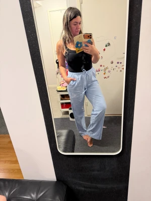 Ljusblå mjukisbyxor med dragsko - Ljusblå byxor med avslappnad passform och elastisk midja med dragsko. Byxorna har raka ben och sidofickor, perfekta för chill dagar. Materialet linne och viskos.Helt nya med prislapp 