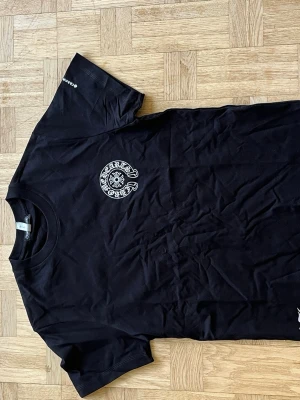 Svart Chrome Hearts t-shirt - Snygg svart t-shirt från Chrome Hearts med stort vitt tryck på ryggen och mindre tryck på bröstet. Klassisk passform med rund hals och korta ärmar. 