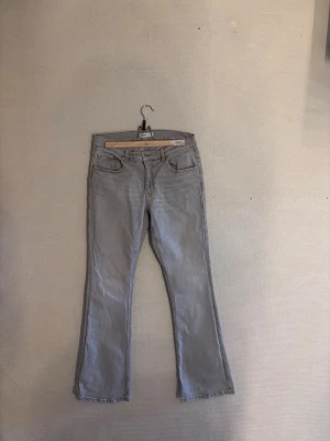 Grå bootcut jeans med låg midja - Snygga grå jeans med bootcut passform och låg midja. Klassisk femficksmodell och dragkedjegylf. Perfekta för en avslappnad och trendig look. Materialet är denim i bomullsblandning.