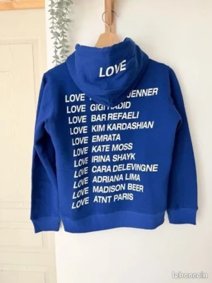 Blå hoodie med vit text LOVE - Cool blå hoodie med vit text på ryggen där det står LOVE följt av olika kända namn. LOVE står även tryckt på huvan. Hoodien har klassisk passform och är perfekt för en avslappnad streetstyle-look.