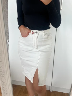 Denim Kjol 🤍 - Snygg vit jeanskjol i klassisk modell med fickor och en cool slits framtill. Kjolen har normal passform och stängs med knapp och dragkedja. Perfekt att matcha med en enkel topp för en clean look. Storlek XS. Stretchig. Fint skick 🩷
