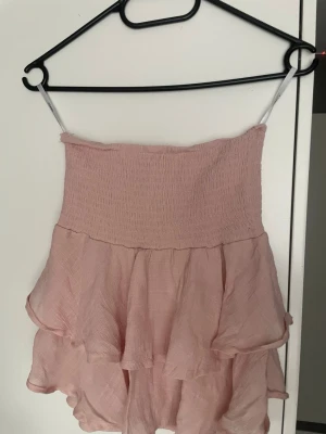 Ljusrosa volangkjol med smock - Supersöt ljusrosa kortkjol med volanger och smockad resårmidja. Kjolen har ett luftigt och lätt material som passar perfekt till varma dagar. 