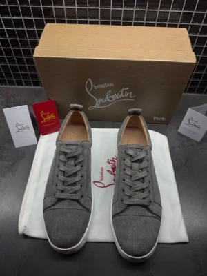 Gråa sneakers från Christian Louboutin 42 - Stilrena gråa sneakers från Christian Louboutin i mocka med vita sulor och klassisk låg profil. Skorna har rund tå, gråa skosnören och diskreta detaljer. Perfekta för dig som gillar exklusiv och minimalistisk design.