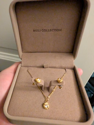 Guldiga örhängen + halsband från Muli Collection - Snygga örhängen i guldton från Muli Collection med gnistrande stenar. De har en rund form och en elegant design som passar perfekt till att lyfta din stil. Perfekt att ge bort som present! Materialet är mässing som är guldpläterad med 18K, med glittrande detaljer som ger en lyxig känsla.