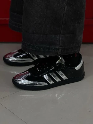 Adidas sneakers i svart och silver - Säljer ett par Adidas sneakers med metallic-silver och svarta paneler, klassiska tre ränder på sidan och svart sula. Skorna har lågt skaft och är tillverkade i syntetmaterial med glansig finish. Perfekta för dig som vill sticka ut med en futuristisk vibe.