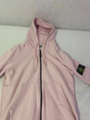 Rosa Stone Island Hoodie/Kofta - Ljusrosa hoodie från Stone Island med dragkedja och klassisk logopatch på vänster ärm.                          Storlek S men passar även M