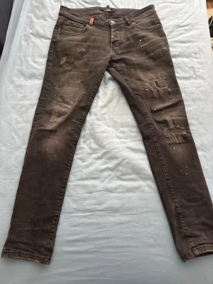 Svarta skinny jeans med slitningar - Säljer ett par svarta skinny jeans med slitningar och distressed detaljer framtill. Jeansen har fem fickor, knappgylf och vita stänk för en trendig look. Passar perfekt till en streetwear-stil och är tillverkade i stretchigt denimtyg. Helt nya, använt 2-3 gånger