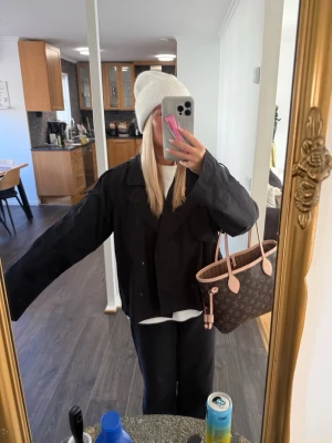 Svart trenchcoat gina - Svart oversized jacka med klassisk krage och knappar framtill. Jackan har en loose passform och är långärmad, perfekt för en avslappnad och trendig look. Passar bra till lager-på-lager och streetwear.
