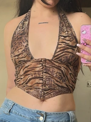 Leopardmönstrad halterneck topp - Snygg croppad halterneck topp med leopardmönster i bruna och beige toner. Djup urringning framtill och knäppning i mitten. Perfekt för dig som vill sticka ut med ett djuriskt mönster.