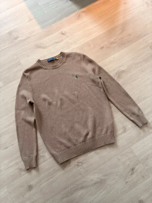 Brun stickad tröja från Polo Ralph Lauren - Brun stickad tröja från Polo Ralph Lauren med rund halsringning och grönt broderat logotyp på bröstet. 
