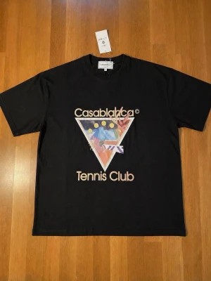 Casablanca Tennis Club t-shirt - Cool svart t-shirt från Casablanca med färgglatt grafiskt tryck och texten 'Tennis Club' på bröstet. Klassisk passform med rund hals och korta ärmar. Perfekt för dig som gillar streetwear och snygga prints.