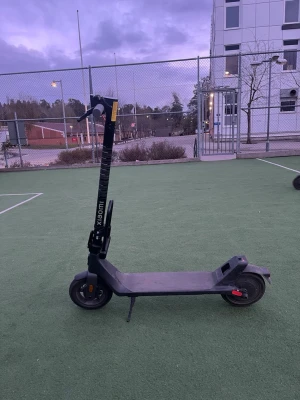 Svart elscooter från Xiaomi - Elektrisk scooter från Xiaomi i svart färg med robust ram och bred ståplatta. Utrustad med handbroms, ringklocka och display på styret. Har röda detaljer på bromskabeln och bakhjulet. Perfekt för smidig transport i stan. Går i 25 km och ingår laddare