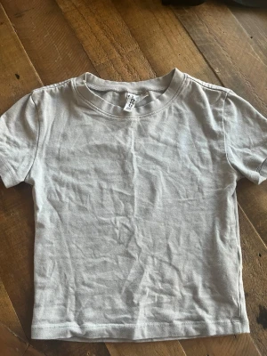 Ljusgrå basic t-shirt från H&M Divided - En enkel och stilren ljusgrå t-shirt från H&M Divided i storlek XS. T-shirten har rund halsringning och korta ärmar, perfekt till alla typer av outfits. Tillverkad i mjuk bomull för skön känsla hela dagen. Köp en t-shirt för 30 styck eller båda för 50 kr