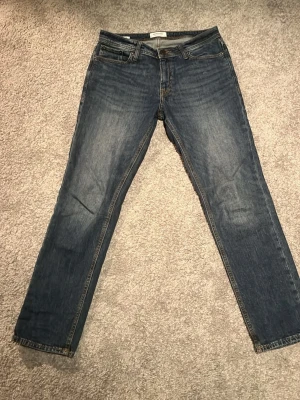 Mörkblå raka jeans från Jack & Jones - Snygga mörkblå jeans från Jack & Jones med klassisk femficksdesign och raka ben. Jeansen har subtila slitningar och kontrastsömmar, tillverkade i bomullsdenim. Perfekta för en avslappnad och stilren look. Storlek: W31 L32