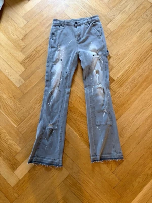 Grå jeans/cargo - Snygga grå jeans  med raka ben, slitna detaljer och råa benslut. Byxorna har flera fickor och coola färgstänk för en trendig, avslappnad look. Perfekta för dig som gillar streetstyle och vill sticka ut lite extra.