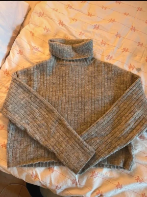 Grå ribbstickad polotröja - Mysig grå ribbstickad polotröja med långa ärmar och hög krage. Tröjan har en avslappnad passform och är tillverkad i ett mjukt material som känns skönt mot huden. Perfekt för kyliga dagar och enkel att matcha med jeans eller kjol.