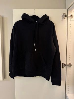 Svart hoodie med magficka och snöre - Svart hoodie i klassisk modell med huva och magficka. Mjuk och bekväm i bomullsblandning – perfekt till vardags. Bra skick! Utan loggor och tryck. 💓