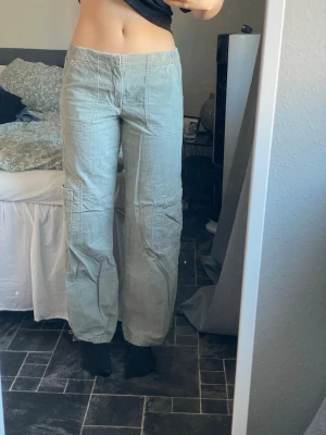 Ljusgröna cargobyxor Pull&Bear - Säljer ett par ljusgrå cargobyxor med avslappnad passform och resår i midjan. Perfekta för en chill och trendig look. Finns snöre vid anklarna som går att dra åt för att skapa ballongform. Använda 1 gång. Är 174cm för referens.
