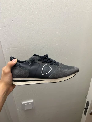 Mörkblåa sneakers med vit detalj - Snygga mörkblåa sneakers med mockaliknande material och vita detaljer på sidan. Skorna har svarta snören och en vit sula med svart rand. Perfekta för en avslappnad och stilren look. Passar till jeans och streetwear.