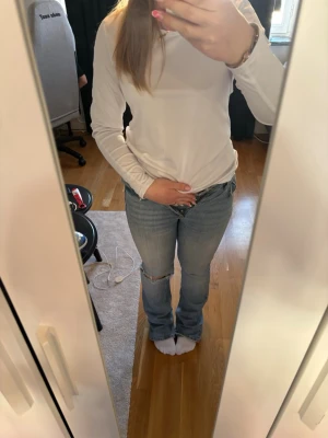 Ljusblå slitna bootcut jeans - Säljer ett par ljusblå jeans med bootcut passform och slitning vid knät. Jeansen har klassisk femficksdesign och normal midja. Perfekta för en avslappnad och trendig look.