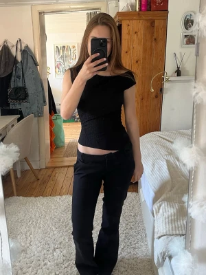 Svart tight topp med asymmetrisk axel - Säljer en svart, tight topp med asymmetrisk axel och croppad passform. Toppen är ärmlös och har en stilren, minimalistisk look som passar perfekt till jeans eller kjol. Materialet känns mjukt och stretchigt, vilket gör den bekväm att bära hela dagen.