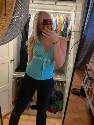 Turkos halternecktopp med knyt - Snygg turkos halternecktopp med knyt runt halsen och djup v-ringning. Toppen är ärmlös och har en croppad passform som visar ryggen. Perfekt för varma dagar och somriga outfits. Köpt secondhand och finns ingen lapp därför vet jag varken märke eller storlek men är av god kvalité och kan passa många storlekar då man knyter.