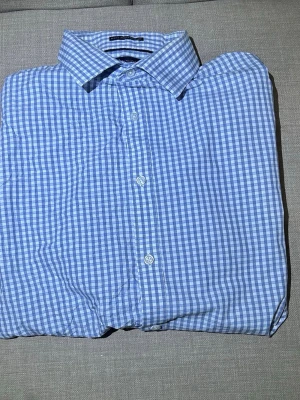 Blårutig skjorta Tommy Hilfiger  - Klassisk blårutig skjorta med vit bas och knappar framtill. Skjortan har en krage och är tillverkad i ett lätt bomullstyg som passar perfekt till vardagslooken. Snygg att bära både öppen och stängd.