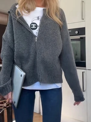 Grå zip hoodie i stickat material - Mysig grå stickad hoodie med dragkedja framtill och avslappnad passform. Tröjan har långa ärmar, ribbade muddar och en stor huva. Perfekt för en chill och casual look.