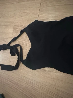 Svart halterneck linnetopp - Snygg svart linnetopp med halterneck och knyt i nacken. Toppen har en lätt v-ringad form och är figurnära med en något utsvängd nederkant. Perfekt att styla med jeans eller kjol för en trendig look.