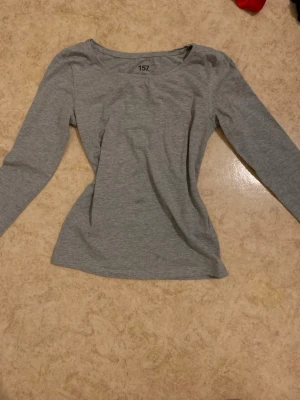 Grå långärmad topp XS - En enkel och stilren grå långärmad topp. Toppen har en rund halsringning och är gjord i mjukt bomullsmaterial som känns skönt mot huden. Perfekt att matcha med jeans eller kjol för en clean look.