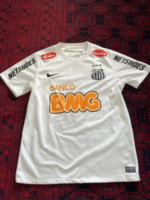 Vit Santos FC matchtröja Nike - Vit Santos FC matchtröja från Nike med tryckta sponsorer och klubbmärke på bröstet. Nummer 11 och Neymar Jr på ryggen. Tröjan har korta ärmar och rund hals, tillverkad i lätt och ventilerande material perfekt för fotboll. Pris kan diskuteras vid snabb och smidig affär 😊😊