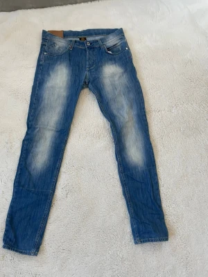 Blå Dondup jeans med slitningar - Snygga blå jeans med slitningar på låren och knäna. Klassisk femficksmodell med knappgylf och kontrastsömmar. Jeansen har en tvättad look och smala ben som ger en modern stil. Perfekta för dig som gillar en avslappnad men trendig outfit.
