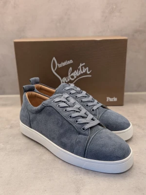 Blå mocka sneakers Christian Louboutin - Snygga blå sneakers i mocka från Christian Louboutin med klassisk röd sula och vita kanter. Skorna har rund tå, matchande blå skosnören och diskreta sömdetaljer. Perfekta för dig som vill ha en exklusiv och stilren look.