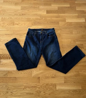 Mörkblå raka jeans från Lee - Säljer ett par klassiska mörkblå jeans från Lee med rak passform. Jeansen har en snygg tvätt och Lee-logga på bakfickan. Perfekta till en avslappnad stil och tillverkade i slitstarkt denimtyg.