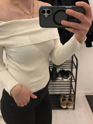 Offshoulder ribbad topp från H&M - Säljer en snygg offshoulder topp från H&M i ribbad, mjuk bomullsblandning. Toppen är vit, har lång ärm och sitter tight för en clean och stilren look. Perfekt att matcha med jeans eller kjol för en trendig outfit.