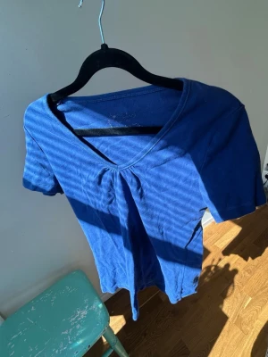 Blå v-ringad topp med kort ärm - En enkel blå topp med v-ringning och korta ärmar. Toppen har en liten rynkdetalj framtill vid halsen och är gjord i mjukt bomullstyg. Perfekt till jeans eller kjol för en avslappnad look🥂