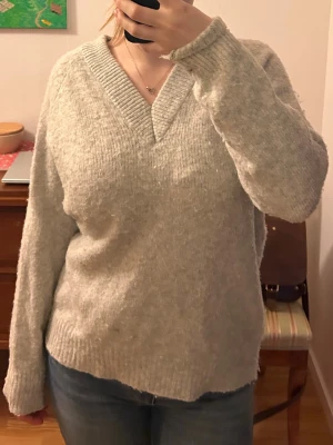 Ljusgrå stickad tröja V-ringad newyorker  - Mysig ljusgrå overzised stickad tröja från New Yorker med V-ringning och ribbade muddar vid ärmslut och nederkant. Tröjan har nopprar.