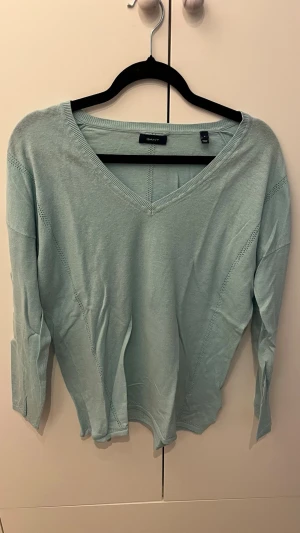 Ljusblå V-ringad tröja från Gant - Snygg ljusblå tröja från Gant med V-ringning och långa ärmar. Tillverkad i ett tunt, mjukt material som känns skönt mot huden. Tröjan har diskreta stickade detaljer längs ärmar och sidor för en stilren look.