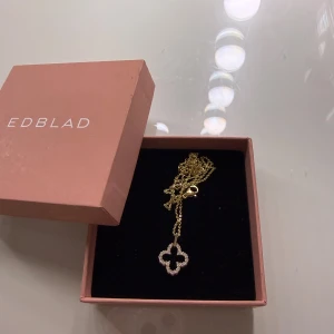 Guldhalsband med fyrklöver  - Säljer ett elegant guldhalsband med ett fyrklöverformat hänge dekorerat med små vita pärlor. Kedjan är tunn och smidig, perfekt för att ge en stilren touch till din outfit. ASK MEDFÖLJER EJ! 