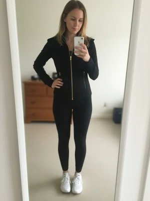 Lulemon set svart - .This iconic Lululemon tracksuit in sleek black is a statement piece for your wardrobe. The set includes a zip-up jacket with gold accents and matching high-waisted leggings. Crafted from a smooth, stretchy material, it offers a flattering fit perfect for both workouts and casual outings. In excellent condition, this set is both functional and fashion-forward, capturing that retro-athleisure vibe.