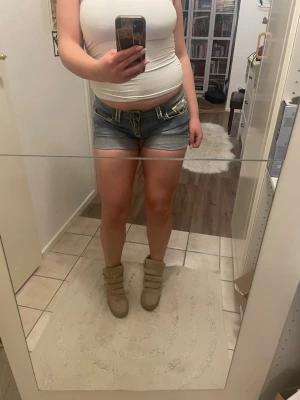 Blå denimshorts från True Religion - Snygga blå denimshorts från True Religion med klassiska kontrastsömmar och detaljerade bakfickor. Modellen är lågmidjad och har en tight passform. Perfekta för varma dagar och enkel att matcha med olika toppar. Jag köpte de här på Plick och personen innan har klippt de från jeans till shorts, så ja har vikt upp de till kortare shorts