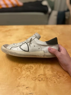 Philippe Model vita sneakers - Snygga vita sneakers från Philippe Model med grå detaljer och svart häl. Skorna har klassisk låg profil, vita skosnören och en ikonisk sidopatch. Tillverkade i läder och mocka för en exklusiv känsla och streetwear-vibe.