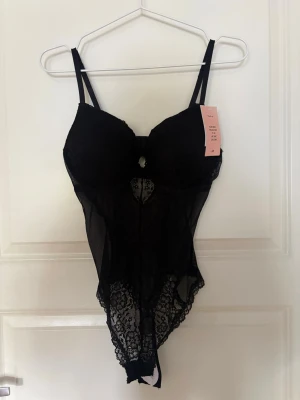 Svart spetsbody från H&M - Slut såld body, aldrig använd!!💓Snygg svart body från H&M med tunna axelband och vadderade kupor. Bodyn är gjord i transparent mesh och spets med blommigt mönster och har en liten öppning framtill. Perfekt för dig som vill ha något extra under kläderna.