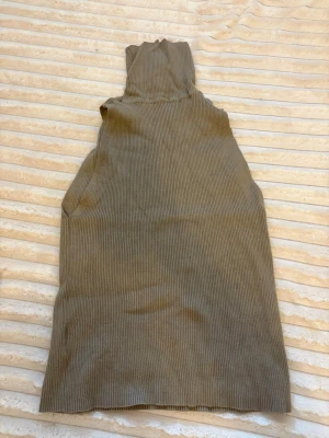 Beige ribbad topp ärmlös - Säljer en beige ribbad topp utan ärmar. Toppen har hög krage och är tillverkad i ett mjukt, stretchigt material som sitter snyggt mot kroppen. Perfekt att styla med jeans eller kjol för en clean look.