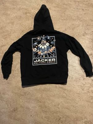 Jacker hoddie ”Political Circus” - En svart hoddie från märket Jacker i storlek M. Trycket ”Jacker Political Circus” pryder plaggets baksida. 