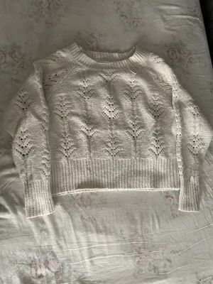 Vit stickad tröja från VILA - Säljer en krämvit stickad tröja från VILA med snyggt hålmönster och bred ribbad kant nedtill och vid ärmsluten. Tröjan har rund halsringning och lång ärm, perfekt för lager på lager och en mysig look.