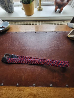 Grisch bälte -  Org pris 249 kr. Snyggt flätat bälte med randigt mönster i rött och blått. Bältet har ett klassiskt metallspänne och detaljer i svart skinn. Perfekt accessoar för att lyfta din outfit med lite färg och stil. Pris kan diskuteras 