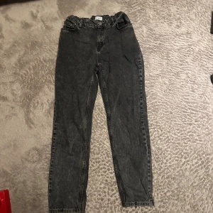 Svarta mom jeans med hög midja - Säljer ett par svarta mom jeans från H&M med hög midja och papperspåse-linning. Jeansen har raka ben och klassiska fickor både fram och bak. Perfekta för en avslappnad och trendig look.